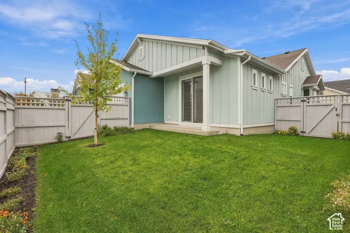 Rear exterior featuring vertical board-and-batten siding, a covered concrete patio, sliding glass door, and a fenced yard with established landscaping