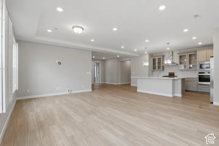 Open floor plan featuring wood-finish flooring, tray ceiling, recessed lighting, and kitchen with a center island, stainless steel built-in appliances, and glass-front cabinetry