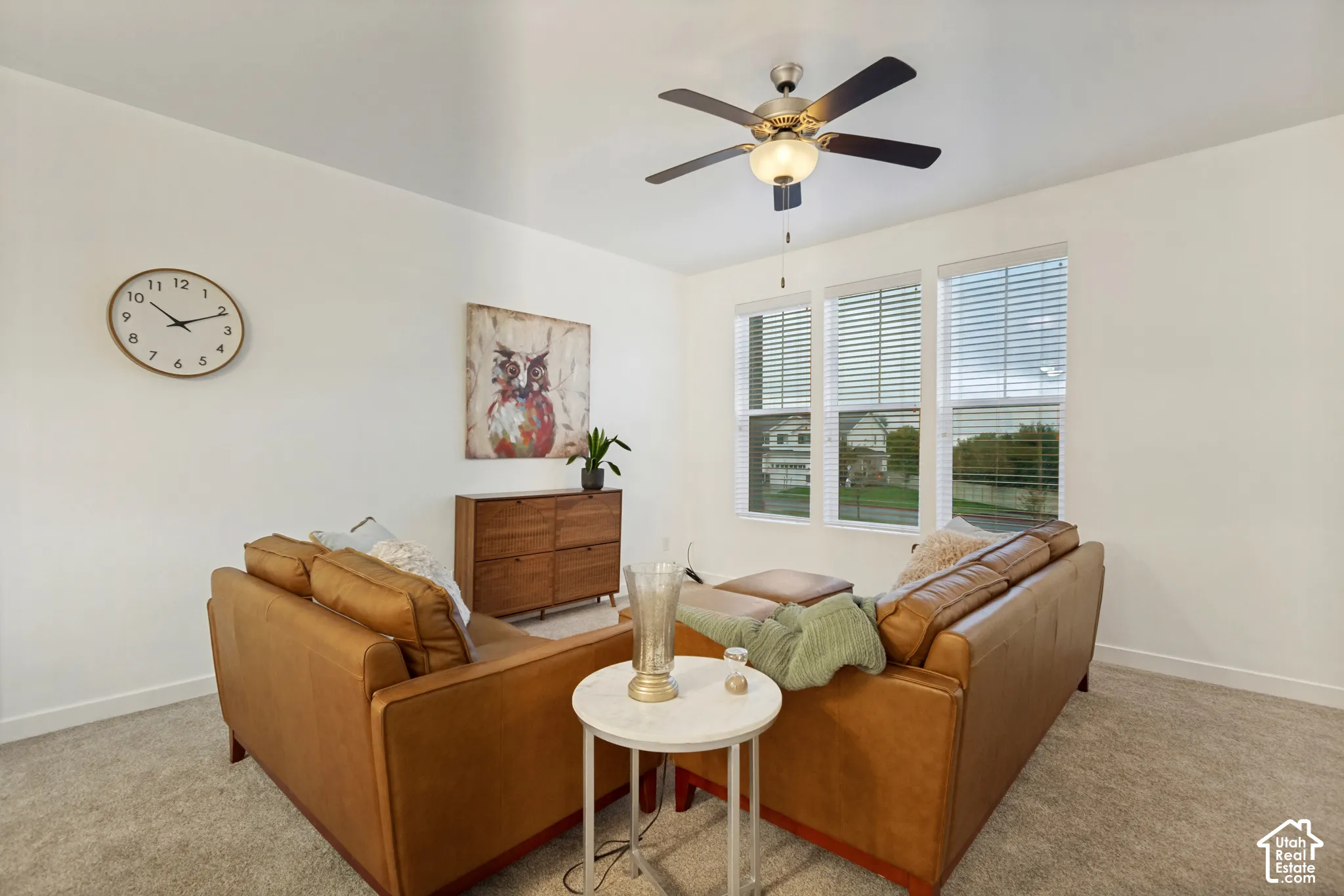 Neutral-toned interior space featuring wall-to-wall carpeting, triple-pane window configuration with integrated blinds, and a multi-blade ceiling fan with central light fixture