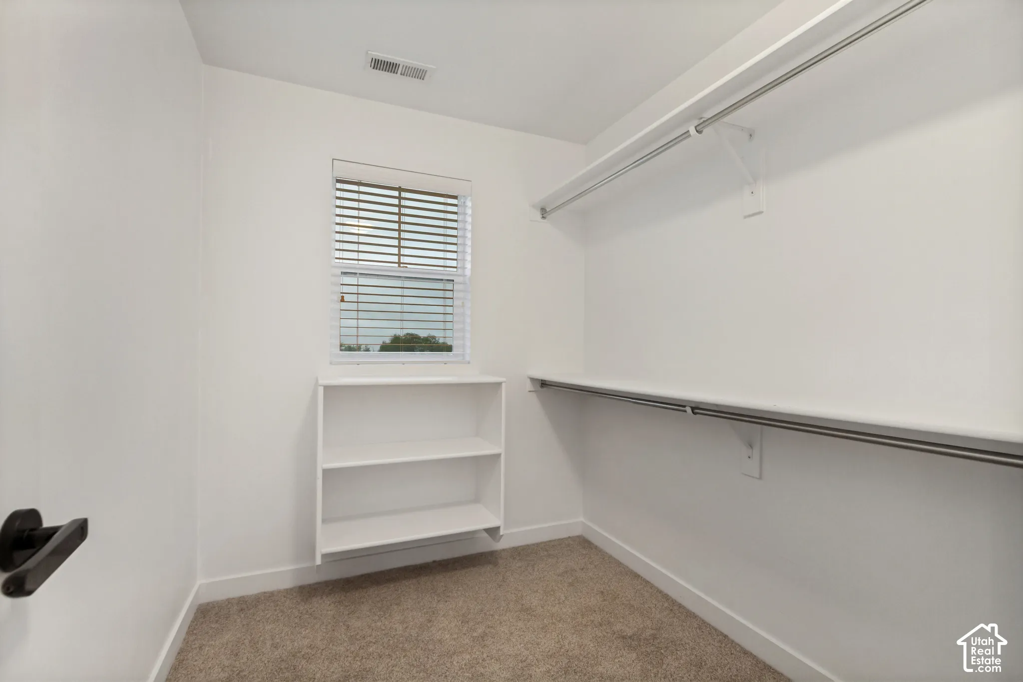 Walk-in closet featuring neutral carpeting, horizontal window blinds, built-in open shelving, and wall-mounted metal clothing rods