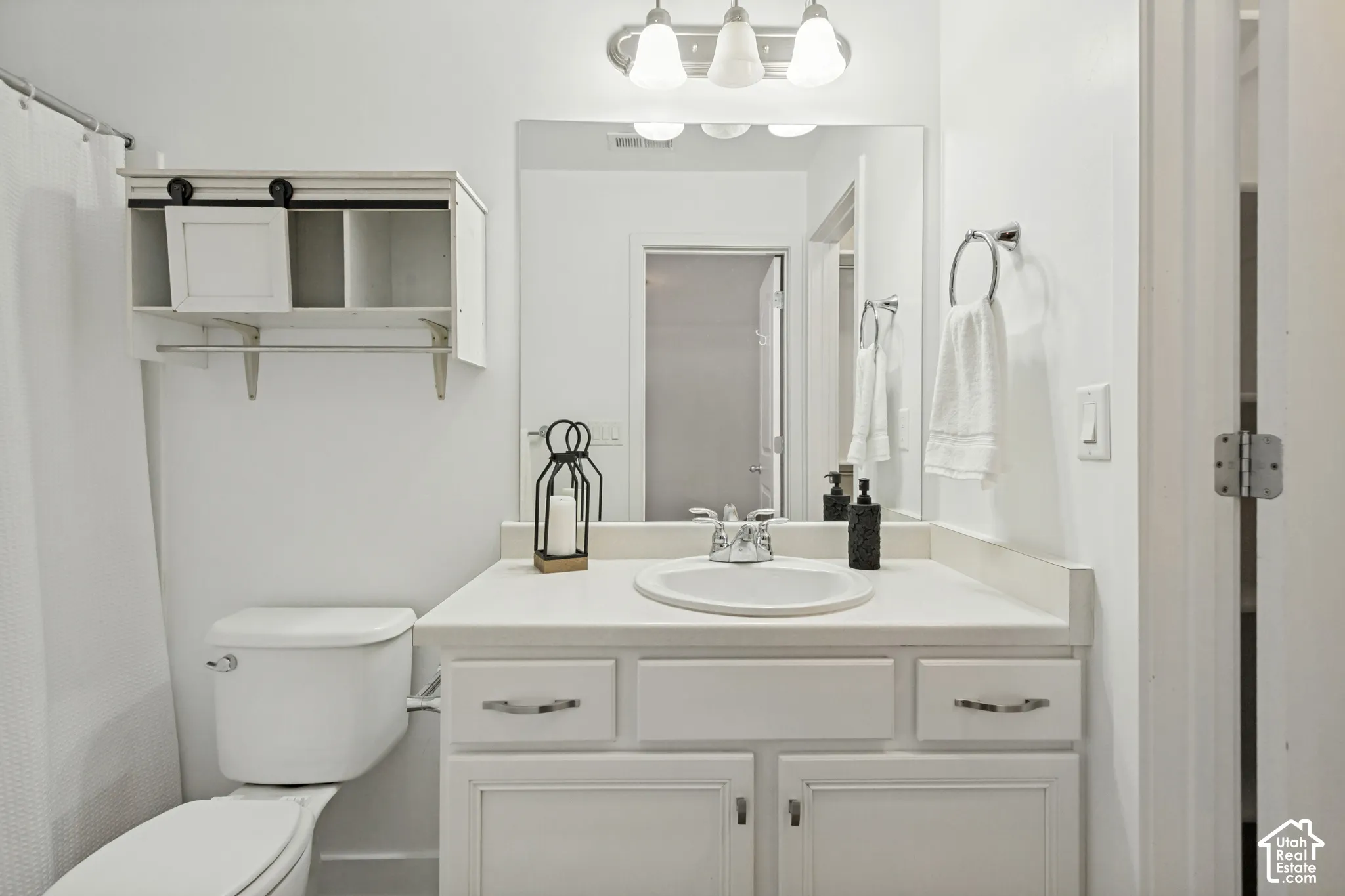 Bathroom featuring a vanity with a white countertop and oval under-mount sink, white cabinetry, a large wall-mounted mirror, three-light overhead fixture, and built-in wall shelving