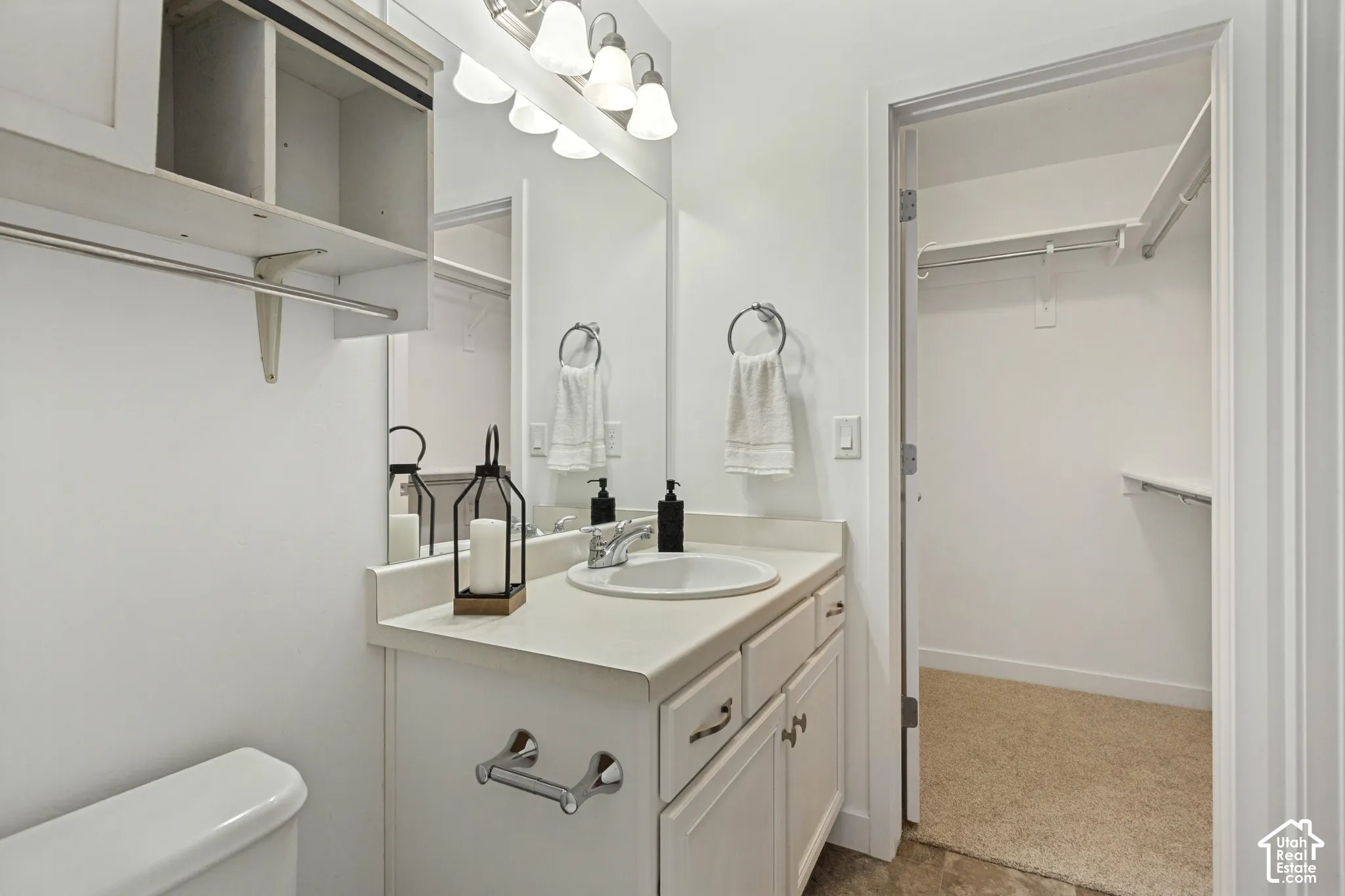 Bathroom featuring a white vanity cabinet, solid-surface countertop with an integrated basin, full-width vanity mirror, four-light fixture, and an internal closet with built-in shelving