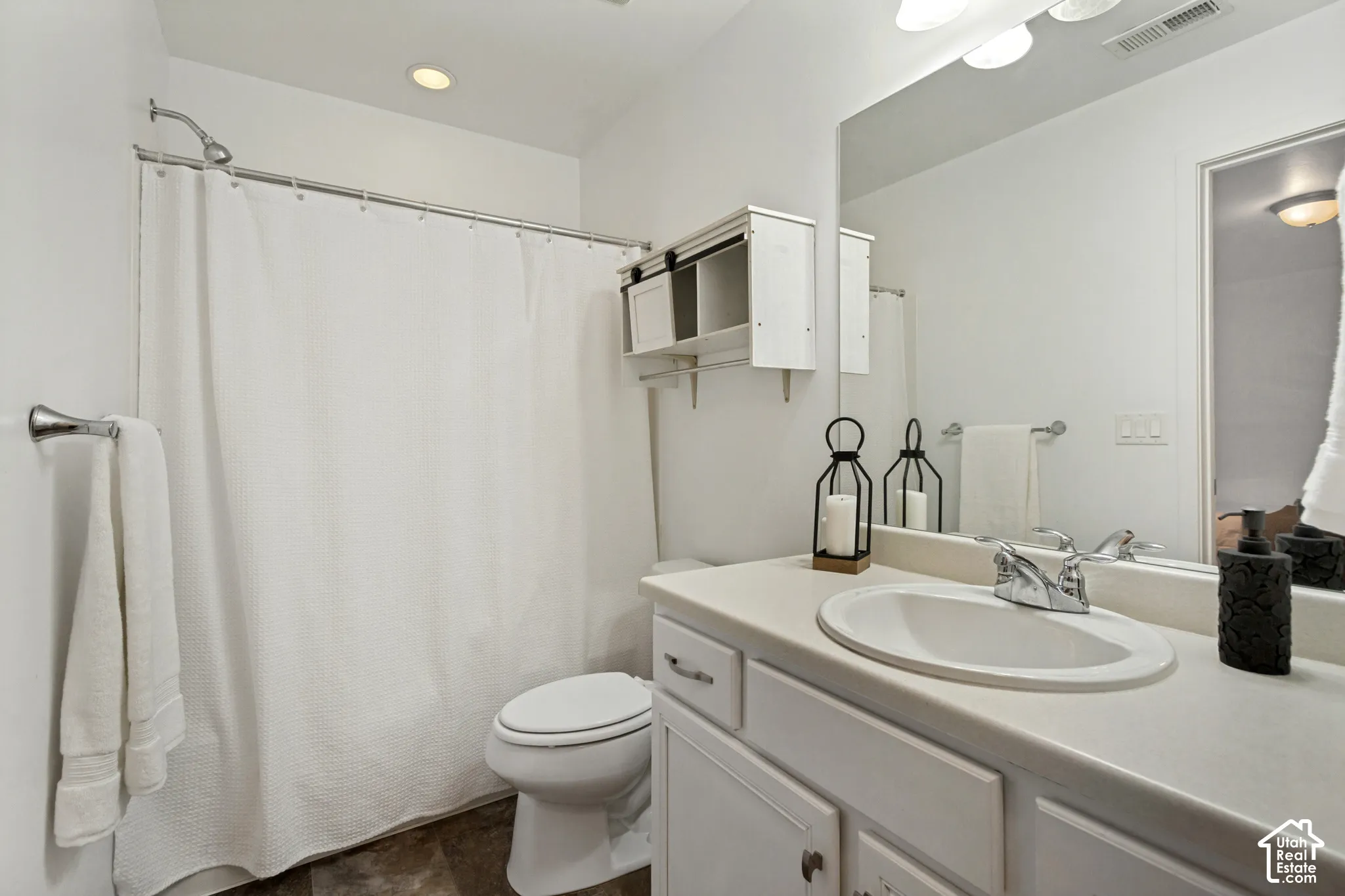 Bathroom featuring a white vanity with a composite countertop and integrated sink, full-width wall mirror, wall-mounted storage cabinetry with sliding doors, and a shower-tub combination with a polished chrome faucet