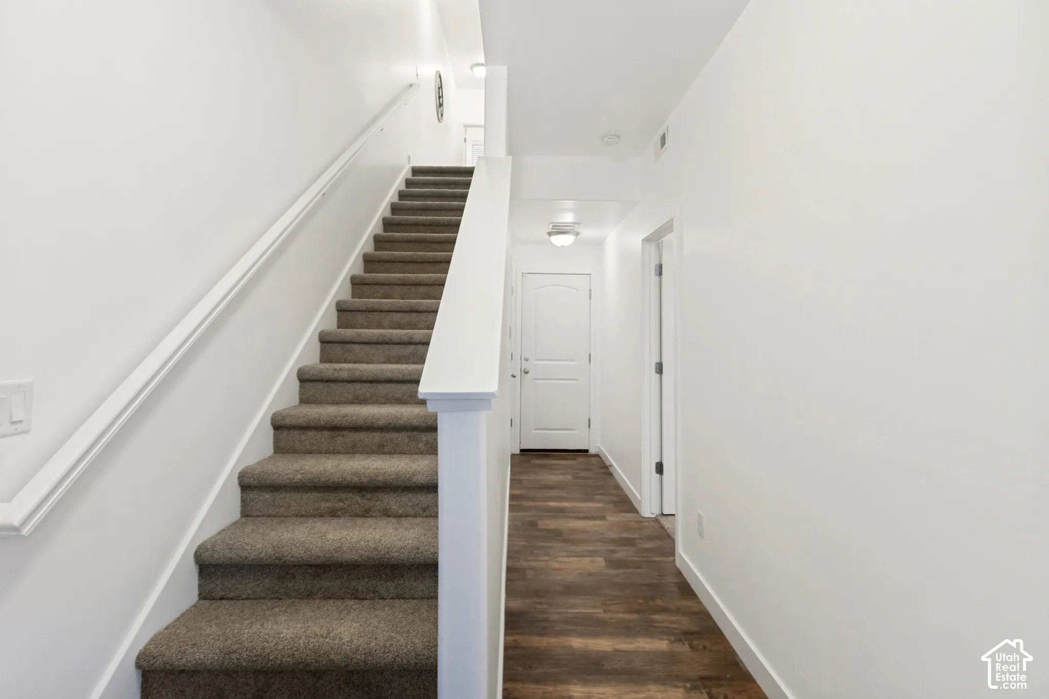 Entryway featuring wood-finish flooring, a carpeted staircase with a white railing, and a paneled interior door with hardware
