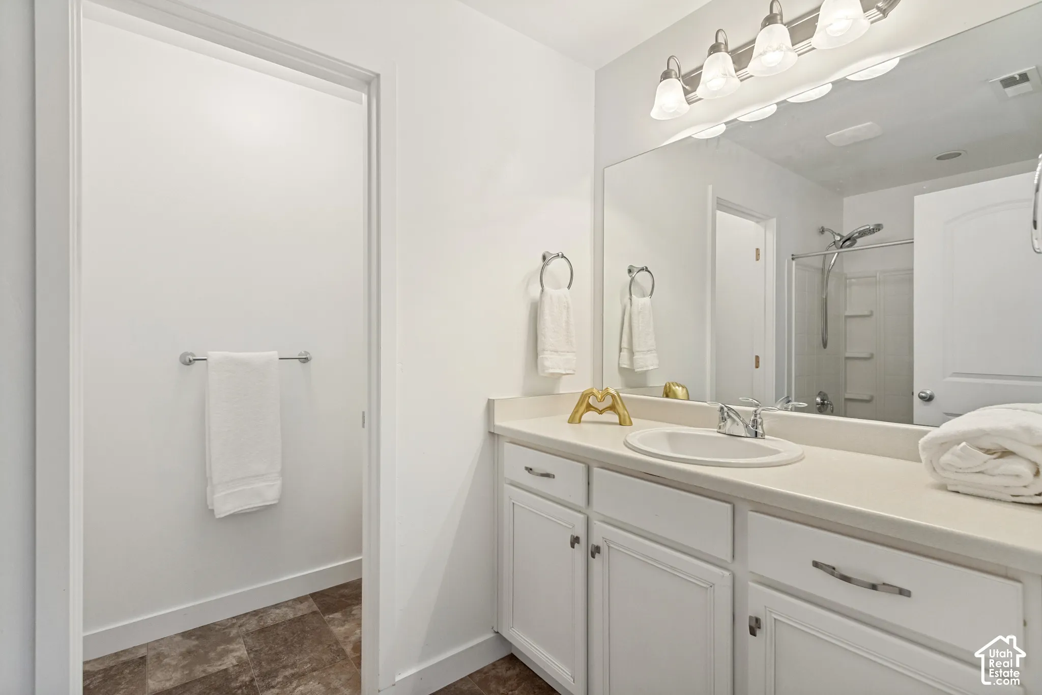 Bathroom vanity featuring white cabinetry, a solid-surface countertop with an integrated oval basin, a full-width mirror, and multi-light wall fixture