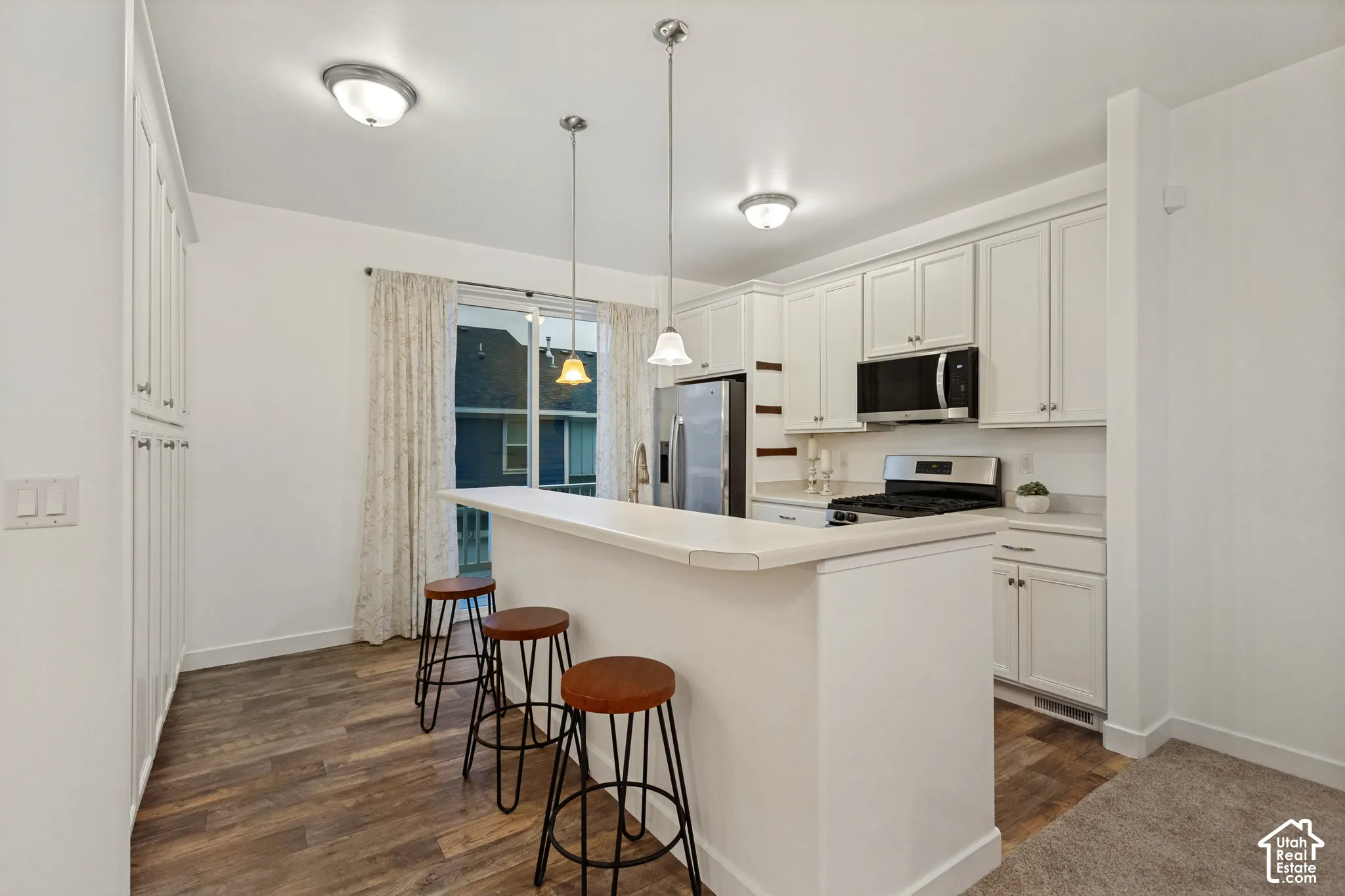 Kitchen featuring white cabinetry, wood-finish flooring, dual hanging pendant lights, stainless steel appliances, and a breakfast bar
