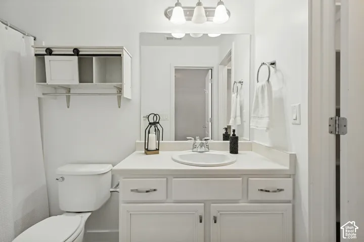 Bathroom featuring a vanity with a white countertop and oval under-mount sink, white cabinetry, a large wall-mounted mirror, three-light overhead fixture, and built-in wall shelving