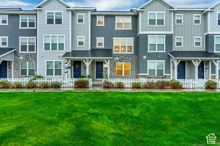 Multi-level townhome exterior featuring stone veneer siding, fiber cement paneling, dual-pitched rooflines, front covered porches with decorative brackets, and white picket fencing