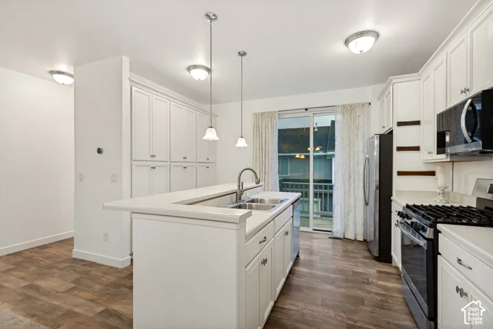 Kitchen featuring white cabinetry, wood-finish flooring, a stainless steel gas range, a multi-level island with an integrated double basin sink, and pendant lighting
