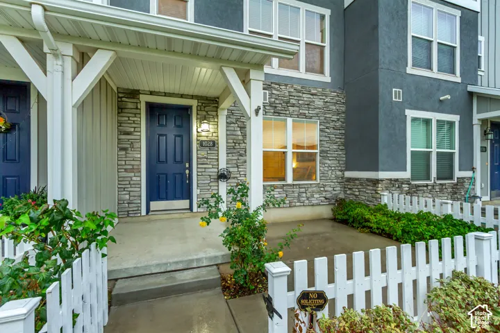 Covered entryway featuring a stone veneer facade, deep blue front door, white picket fencing, and multi-pane windows with grid detailing