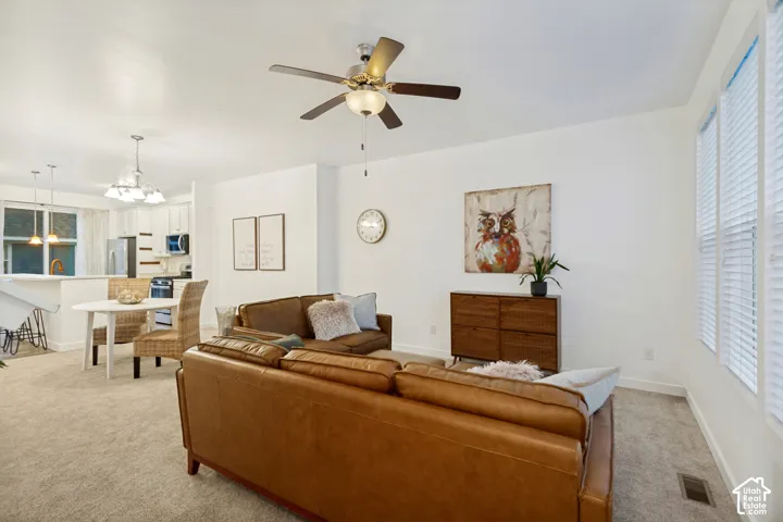 Open-concept interior featuring neutral wall tones, wall-to-wall carpeting, a multi-blade ceiling fan with integrated lighting, and white-framed windows with horizontal blinds