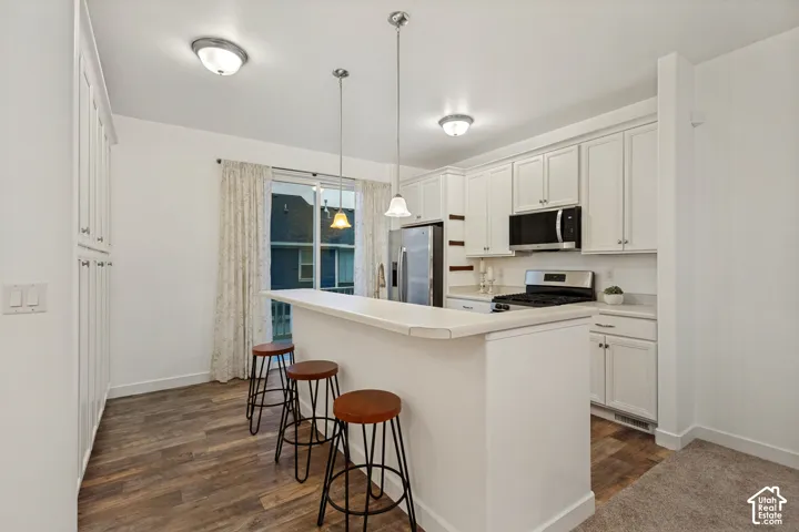 Kitchen featuring white cabinetry, wood-finish flooring, dual hanging pendant lights, stainless steel appliances, and a breakfast bar