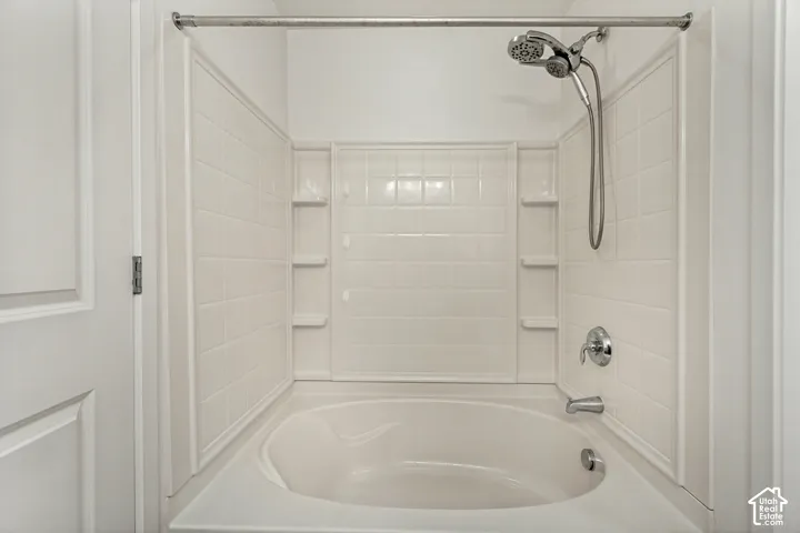 Built-in soaking tub with a tiled surround, integrated shelving, handheld shower fixture, and a metal shower rod