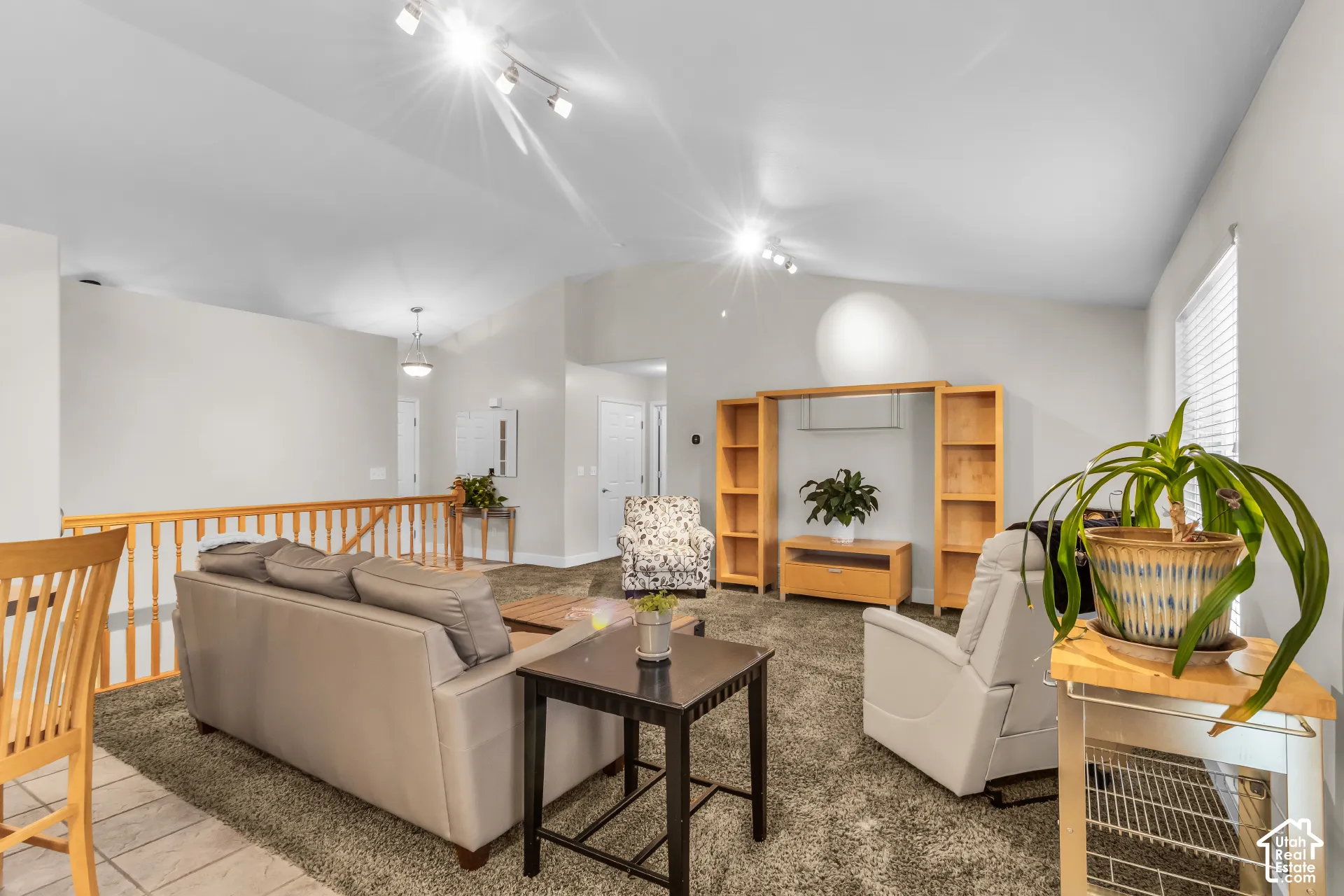 Vaulted ceilings, built-in wooden shelving, track lighting, and wood-finish railings