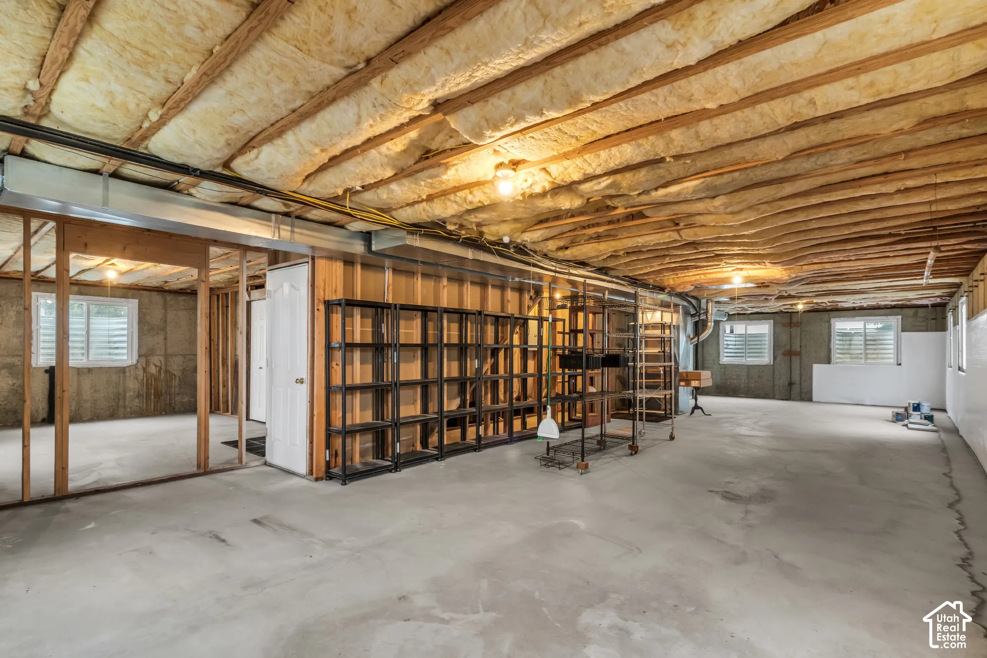 Unfinished basement area featuring exposed timber framing, concrete flooring, glass block windows, and fiberglass batt insulation
