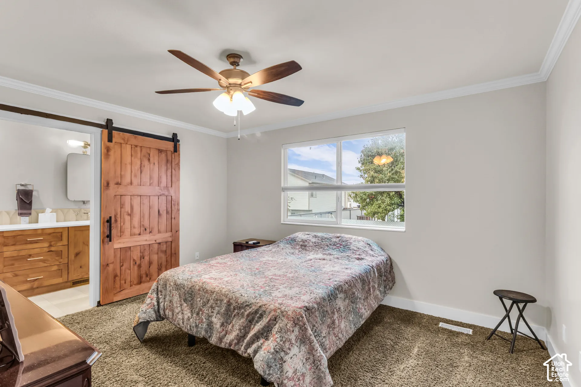 Bedroom featuring a sliding wood barn door, crown molding, a central ceiling fan with integrated lighting, and a large window