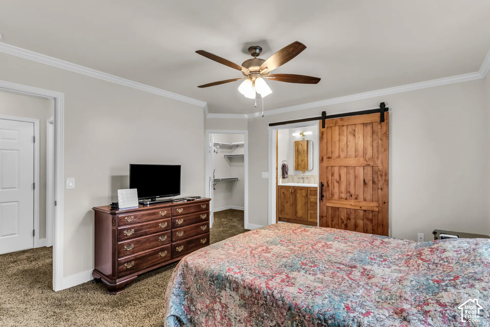 Interior room featuring a natural wood sliding barn door, crown molding, and a central ceiling fan with integrated lighting