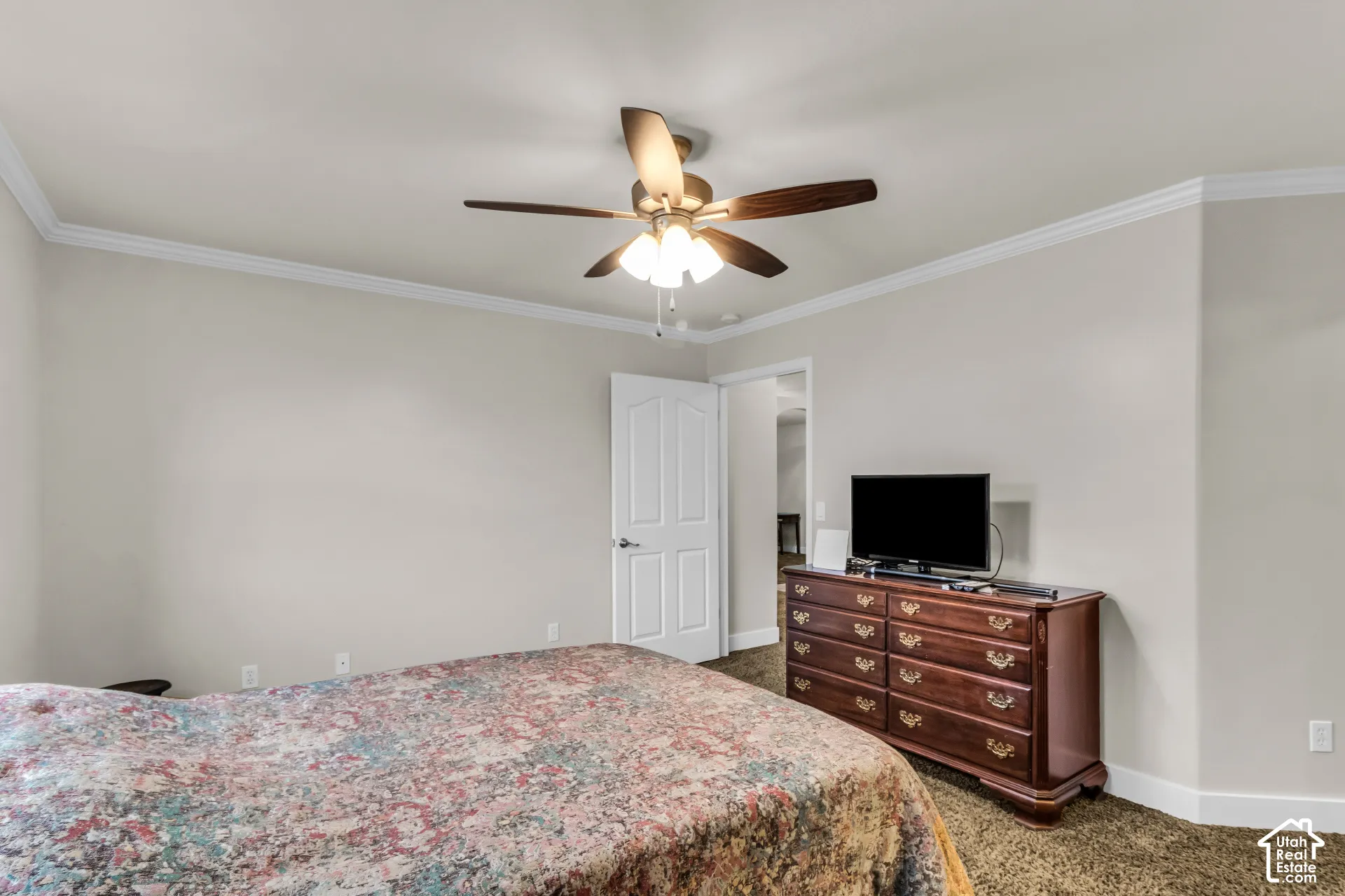Neutral-toned interior space featuring crown molding, a central ceiling fan with multi-light fixture, and a multi-panel interior door