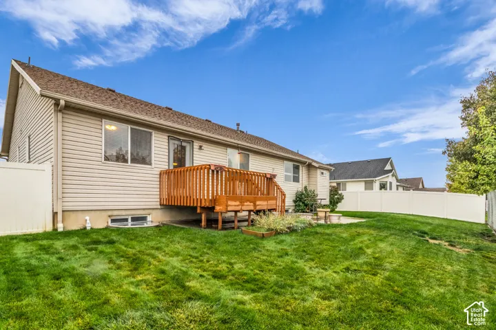 Rear exterior featuring horizontal vinyl siding, wood deck with balustrades, concrete patio, and white vinyl privacy fencing enclosing the lawn