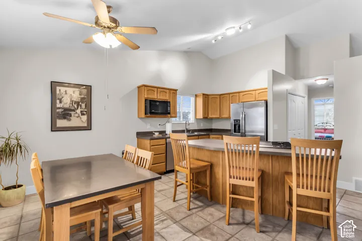 Kitchen featuring vaulted ceilings, wood cabinetry, a central island with counter seating, stainless steel appliances, and ceramic tile flooring