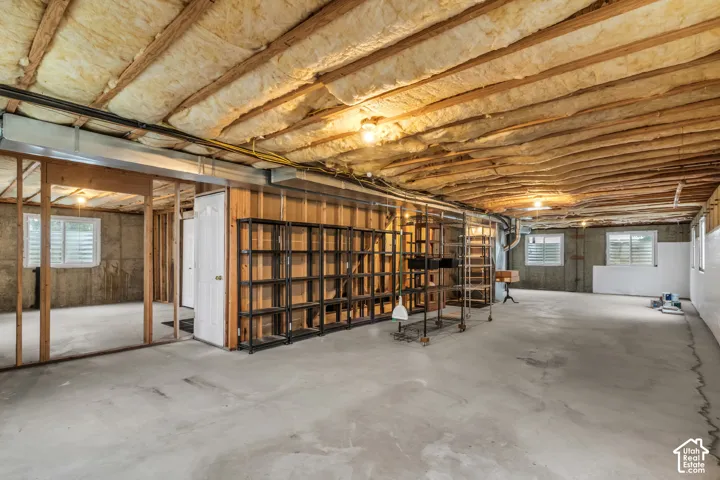 Unfinished basement area featuring exposed timber framing, concrete flooring, glass block windows, and fiberglass batt insulation