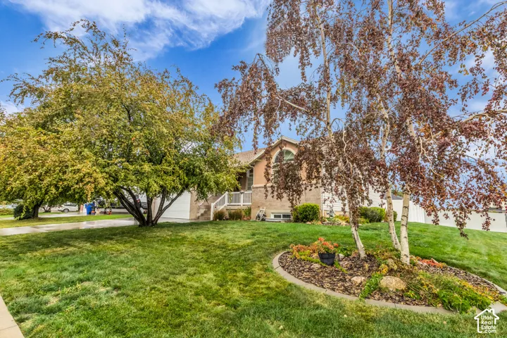 Exterior facade featuring brick masonry and stucco siding, arched window detail, manicured lawn, established trees, and stone-bordered landscaping beds