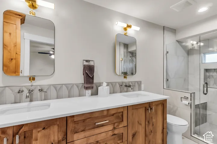 Dual-sink vanity with wood cabinetry, white countertops, wall-mounted faucets, arched mirrors, and a glass-enclosed shower with tile surround