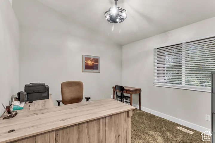 Vaulted ceiling room featuring neutral wall paint, textile carpeting, a large window with horizontal blinds, and a circular geometric chandelier