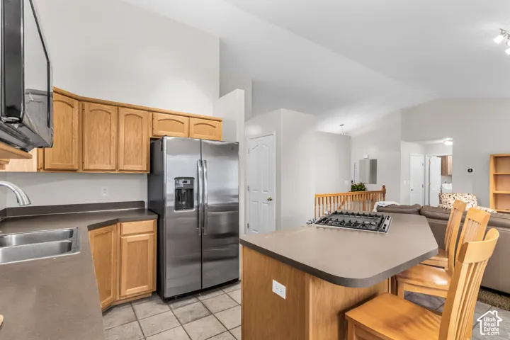 Kitchen featuring vaulted ceilings, wood cabinetry, a stainless steel refrigerator, an integrated gas cooktop on the island, and tile flooring
