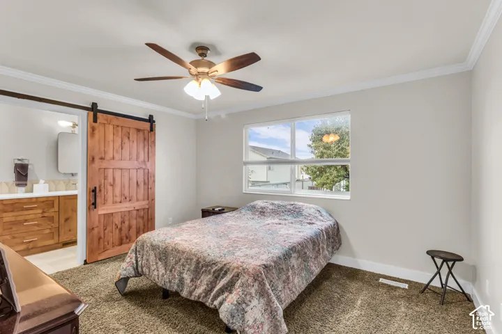 Bedroom featuring a sliding wood barn door, crown molding, a central ceiling fan with integrated lighting, and a large window