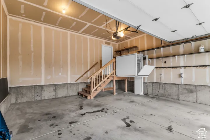 Multi-car garage featuring a concrete floor, built-in wooden staircase, wall-mounted shelving, and a vertical platform lift