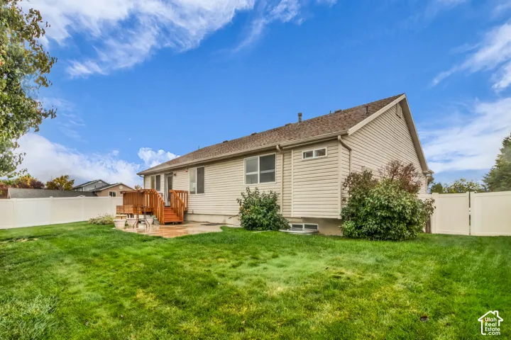 Expansive backyard featuring a manicured lawn, wood-construction deck, concrete patio, and white vinyl perimeter fencing