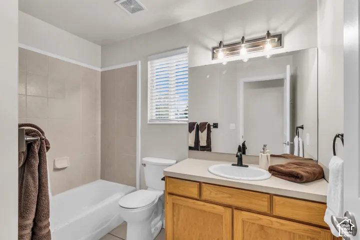 Bathroom featuring a wood-finish vanity with a solid-surface countertop, integrated basin, matte black hardware, and a tub-shower combination with ceramic tile surround