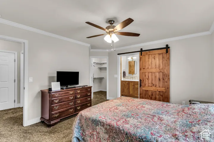Interior room featuring a natural wood sliding barn door, crown molding, and a central ceiling fan with integrated lighting