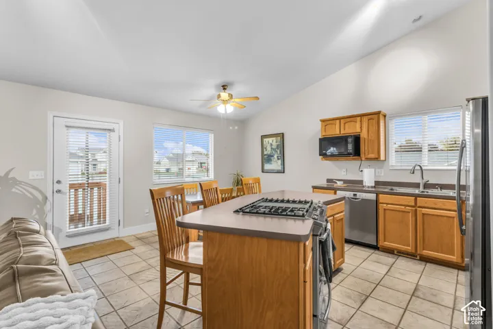 Kitchen featuring shaker-style wood cabinetry, central island with a built-in gas cooktop, tile flooring, vaulted ceiling, and glass-paneled exterior door