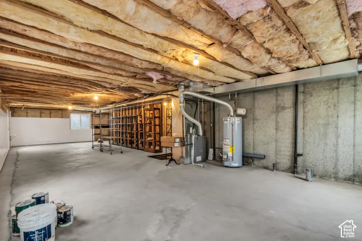 Unfinished basement space featuring a poured concrete floor, exposed ceiling joists with fiberglass insulation, concrete foundation walls, and a dedicated water heater