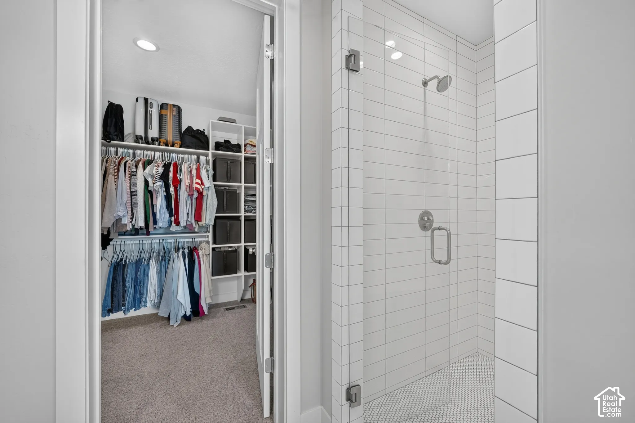 Walk-in closet featuring white built-in shelving, complemented by a tiled shower with a frameless glass door and polished chrome hardware