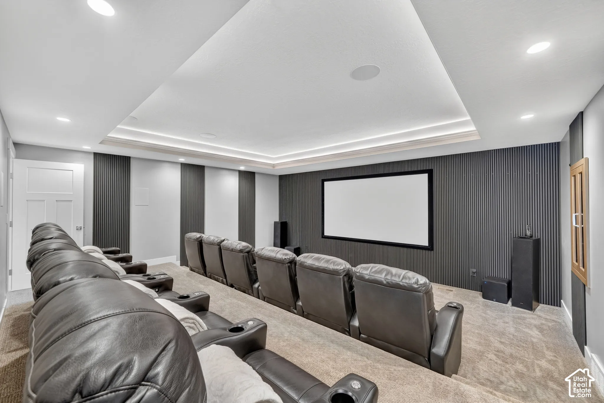 Media room featuring a recessed tray ceiling, integrated cove lighting, vertical slat wall paneling, and a built-in projection screen