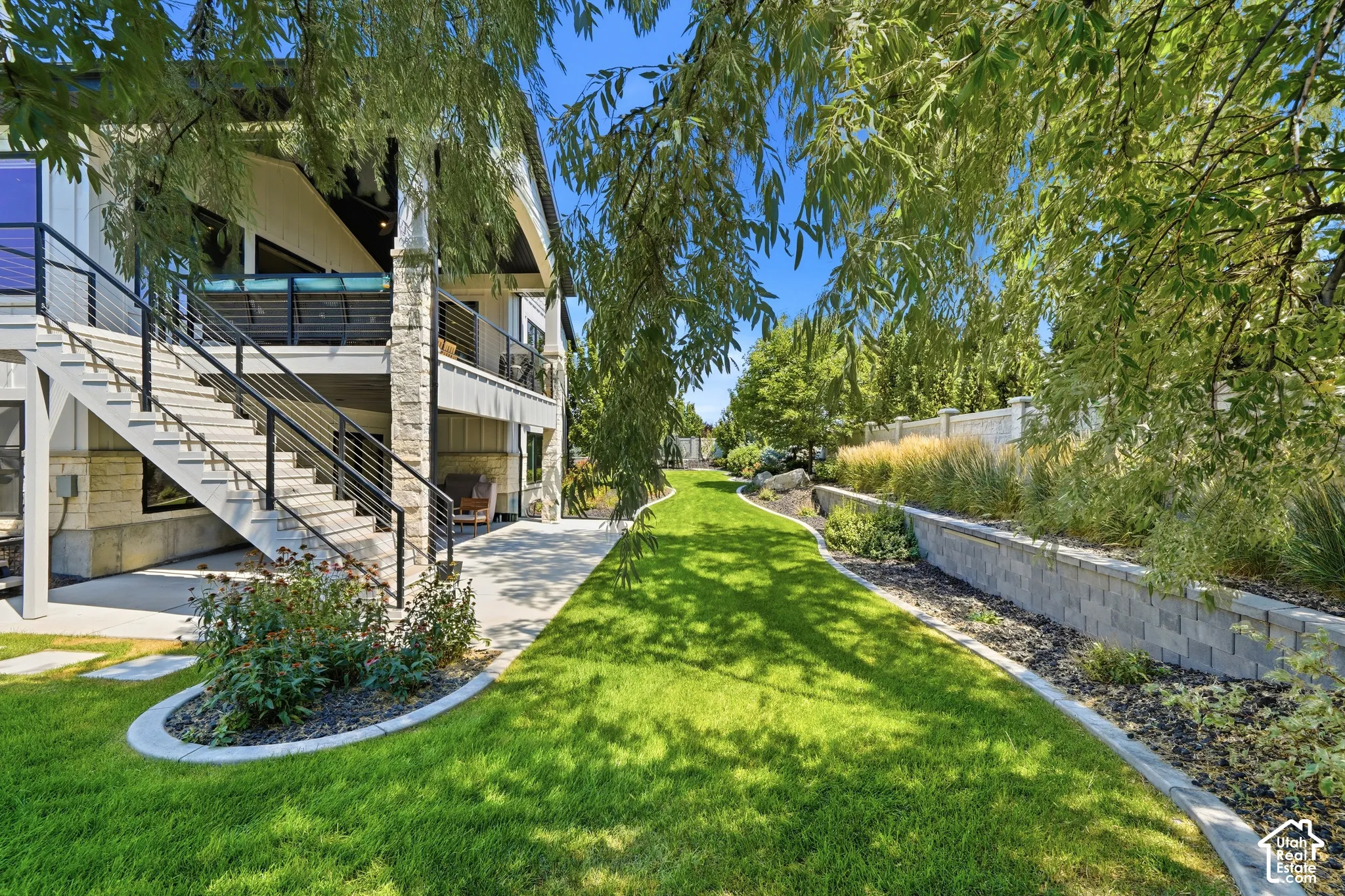 Backyard featuring a concrete patio, stone-veneer column supports, exterior staircase with metal railings, and a terraced retaining wall