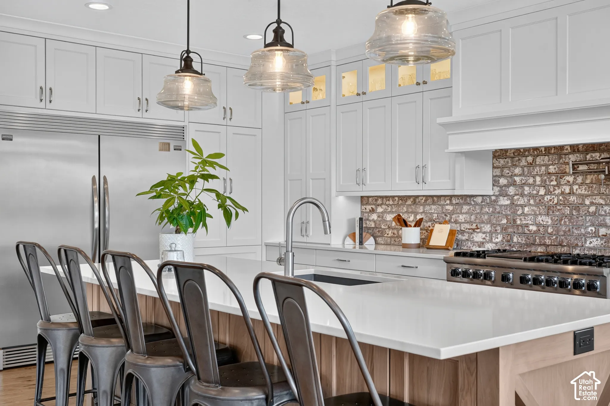 Kitchen featuring white cabinetry with glass-front uppers, a central island with a stone countertop, an exposed brick backsplash, recessed lighting, and industrial-style pendant fixtures