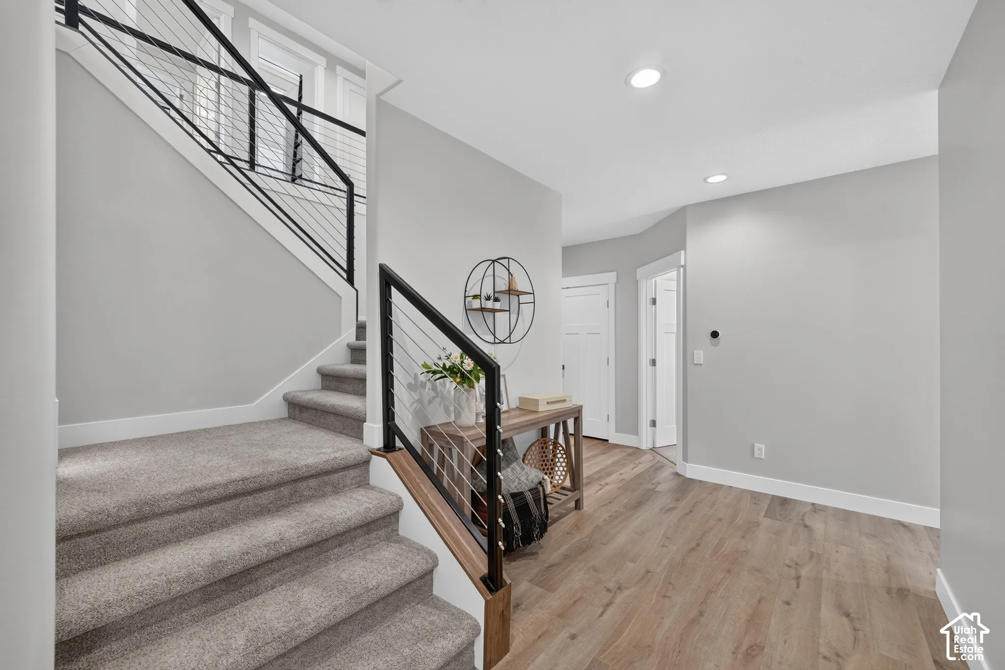 Staircase featuring a black metal railing with horizontal cable infill and wood-finish flooring