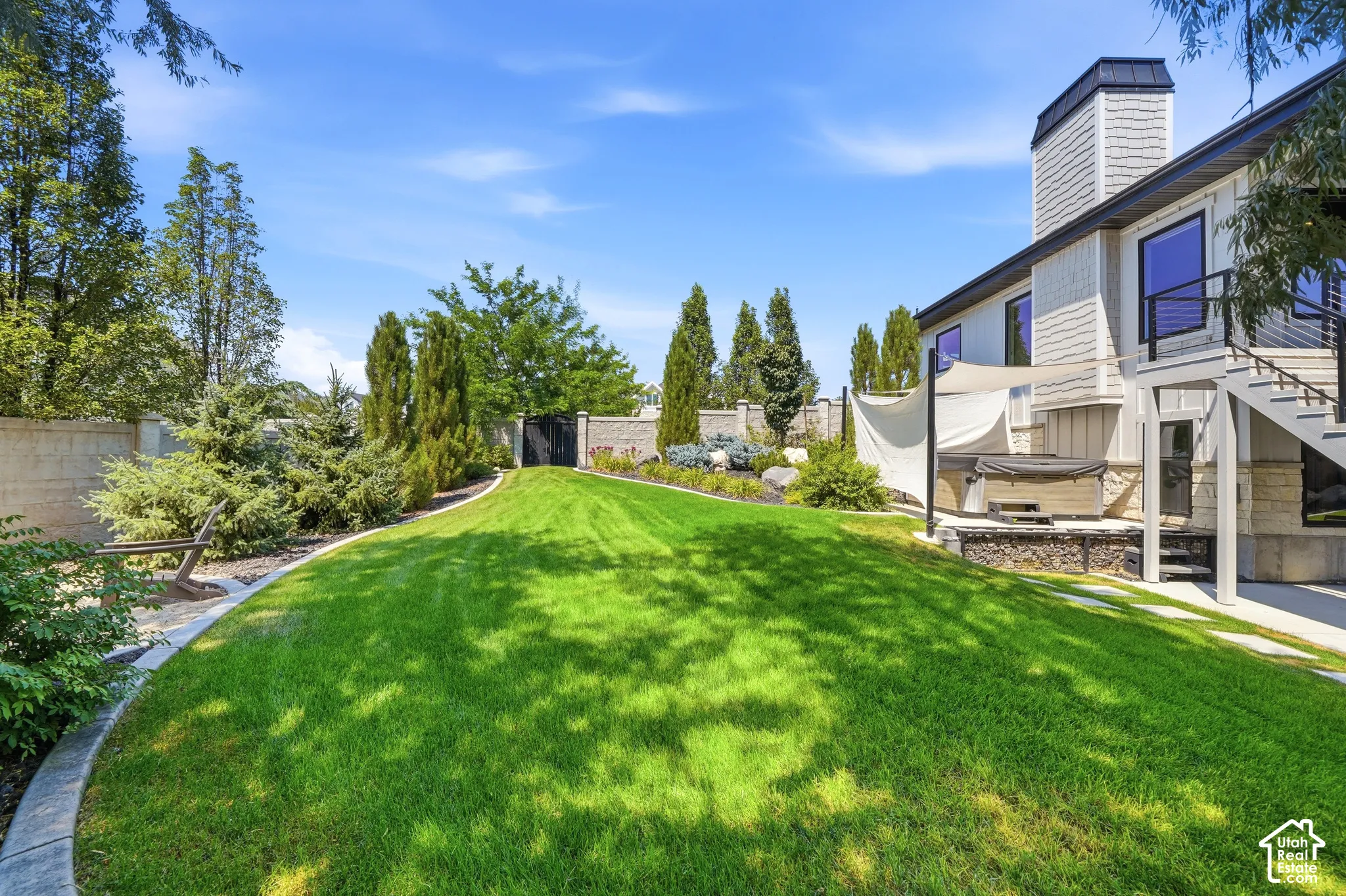 Private backyard featuring a manicured lawn, stone perimeter wall, stone-accented exterior foundation, stone paver pathway, and mature landscaping