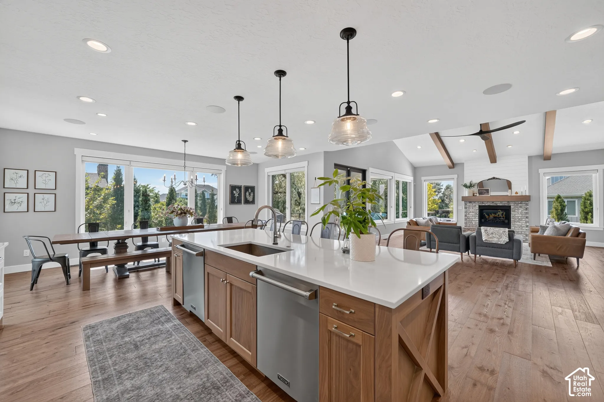 Open-concept kitchen featuring an oversized island with quartz countertops, custom wood-finish cabinetry, stainless steel appliances, pendant lighting, and wide-plank wood-finish flooring