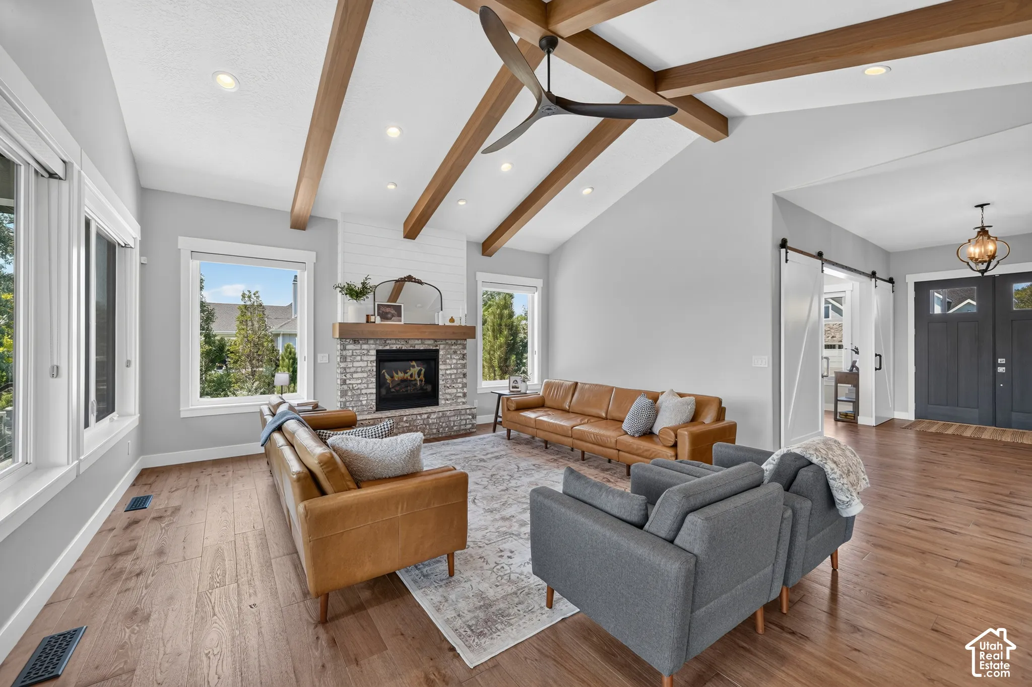 Living area featuring vaulted ceilings with exposed wood beams, wood-finish flooring, recessed lighting, and a stone-surround fireplace with a wood mantel