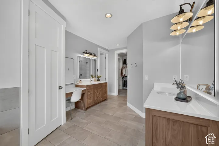 Dual wooden vanities with white countertops, integrated sinks, large plate glass mirrors, multi-light fixtures, and tile flooring