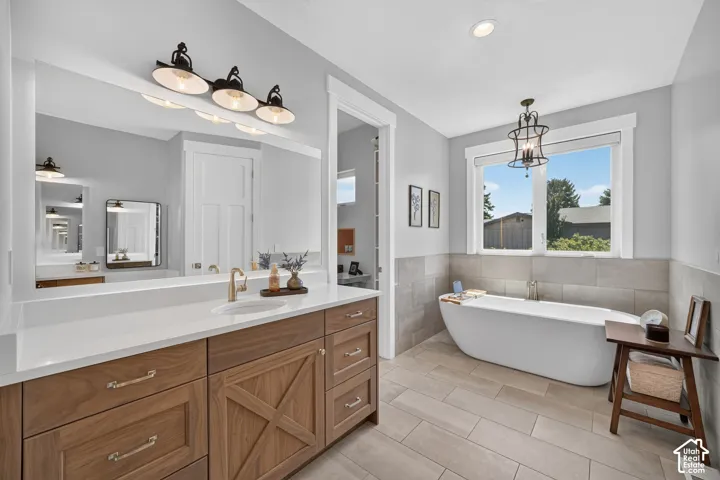 Bathroom featuring a custom wood vanity with X-panel detailing, white surface countertop, freestanding soaking tub, neutral tile flooring, and metallic light fixtures