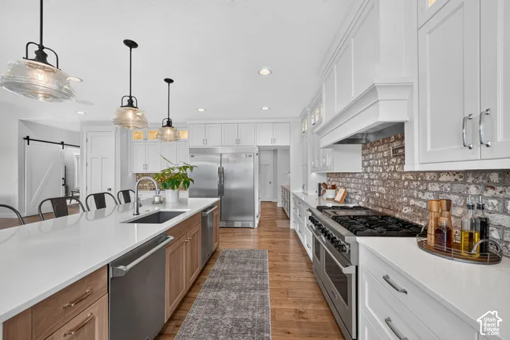 Kitchen featuring a large central island with quartz countertops, custom white and wood-finish cabinetry, a professional-grade stainless steel range, exposed brick backsplash, and decorative pendant lighting