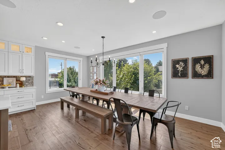Dining area featuring wood-finish flooring, white built-in cabinetry, recessed lighting, a multi-arm chandelier, and large windows
