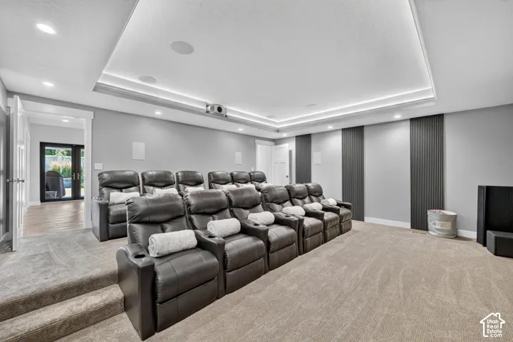 Tray ceiling featuring recessed perimeter lighting, multi-level tiered flooring, integrated ceiling speakers, and vertical slat wall paneling