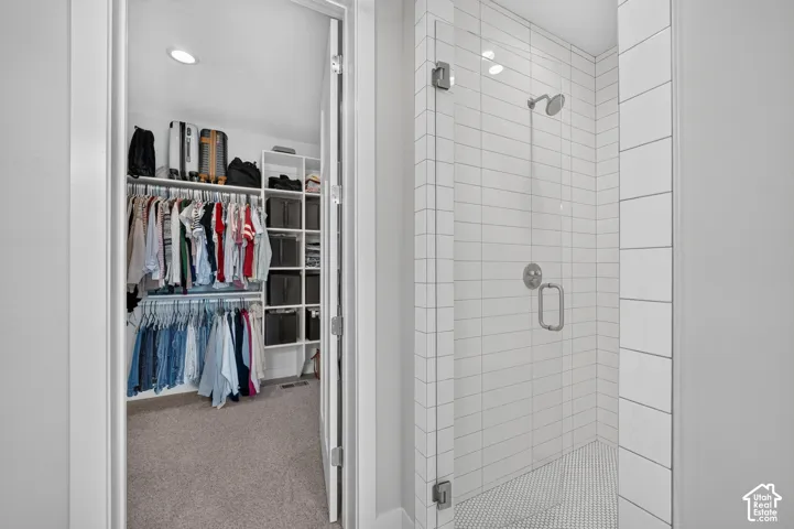 Walk-in closet featuring white built-in shelving, complemented by a tiled shower with a frameless glass door and polished chrome hardware